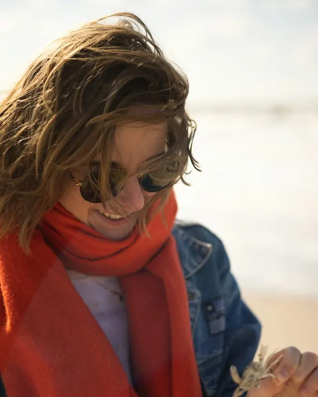 A woman in an orange scarf laughing on a windy beach